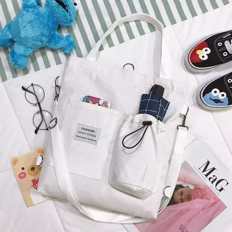 White tote bag with a small umbrella, surrounded by various items including a blue plush toy and shoes on a striped background.