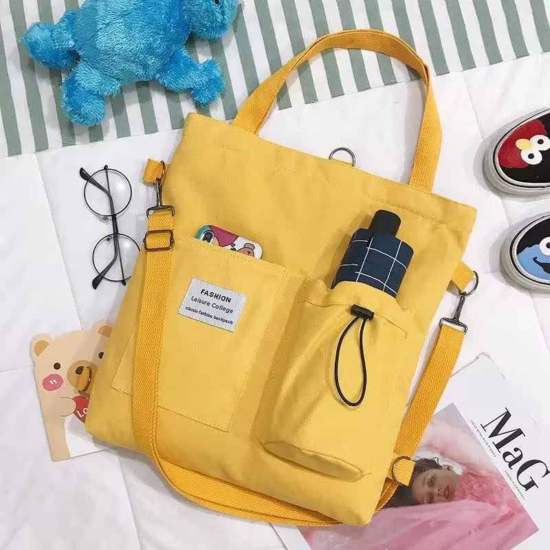 Yellow bag with a strap on a surface with various items including a blue toy and glasses.