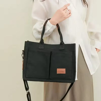 Black handbag held by a person wearing a white shirt against a neutral background