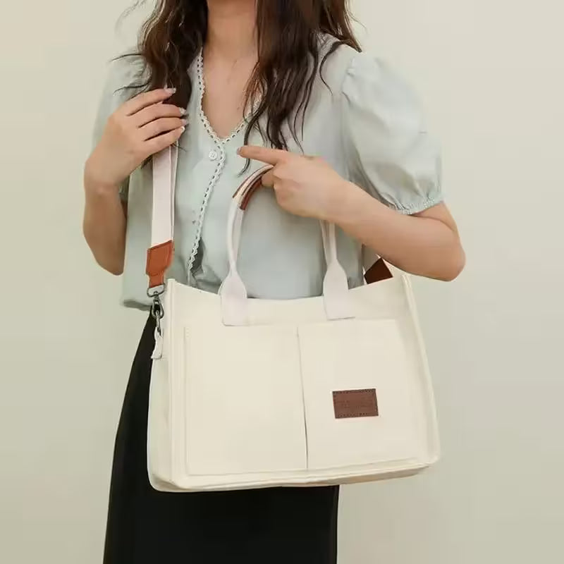 Woman holding a white tote bag with a brown strap against a plain background