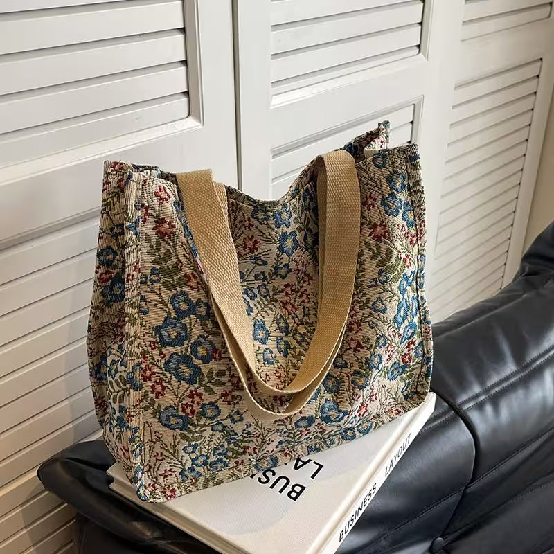 Floral-patterned tote bag with beige handles on a black surface.