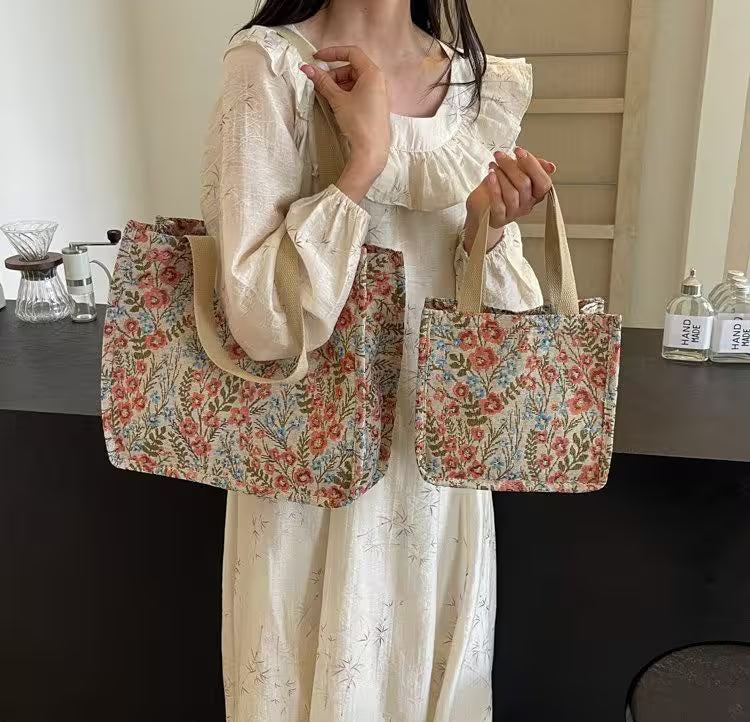 Person holding two floral-patterned bags in a room with a table and bottles in the background.