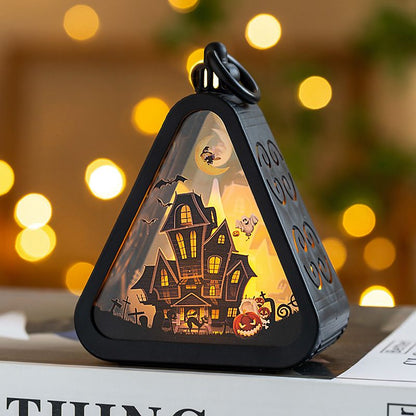 Halloween-themed light-up house model with glowing interior against a blurred festive background.