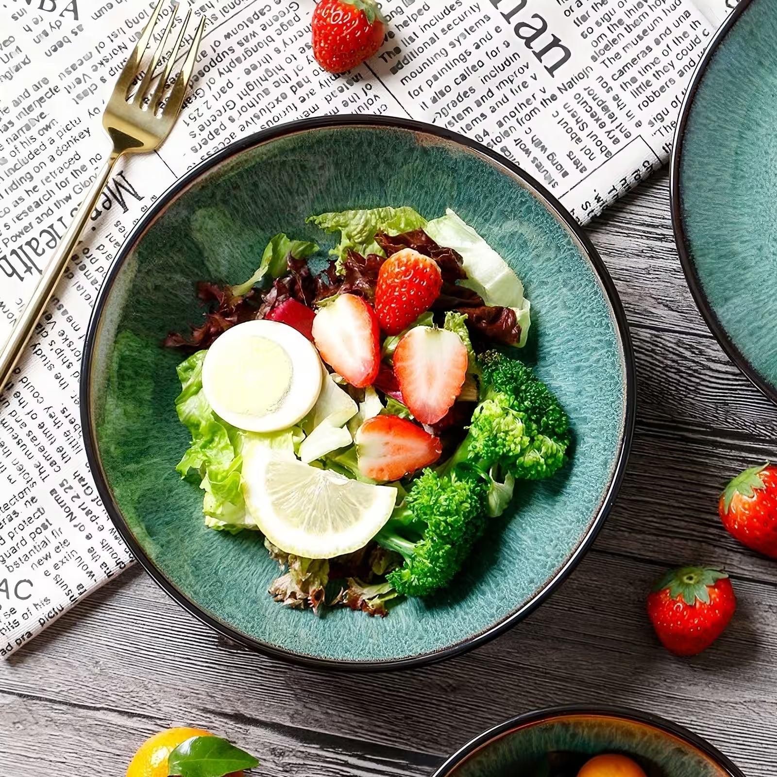 Green salad with strawberries and broccoli on a blue plate, placed on a newspaper.