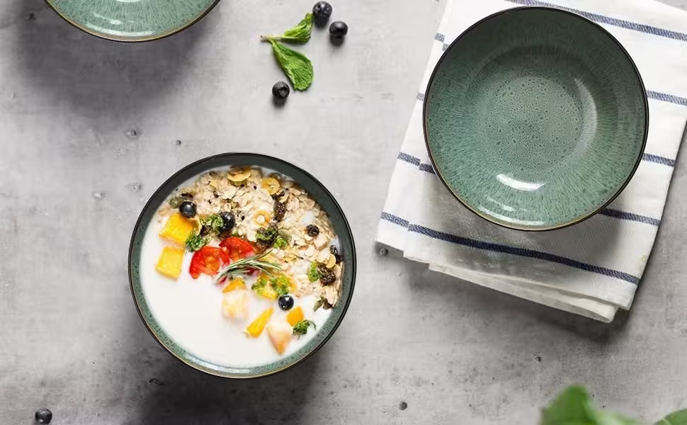 Bowl of oatmeal with fruits and a green plate on a gray surface