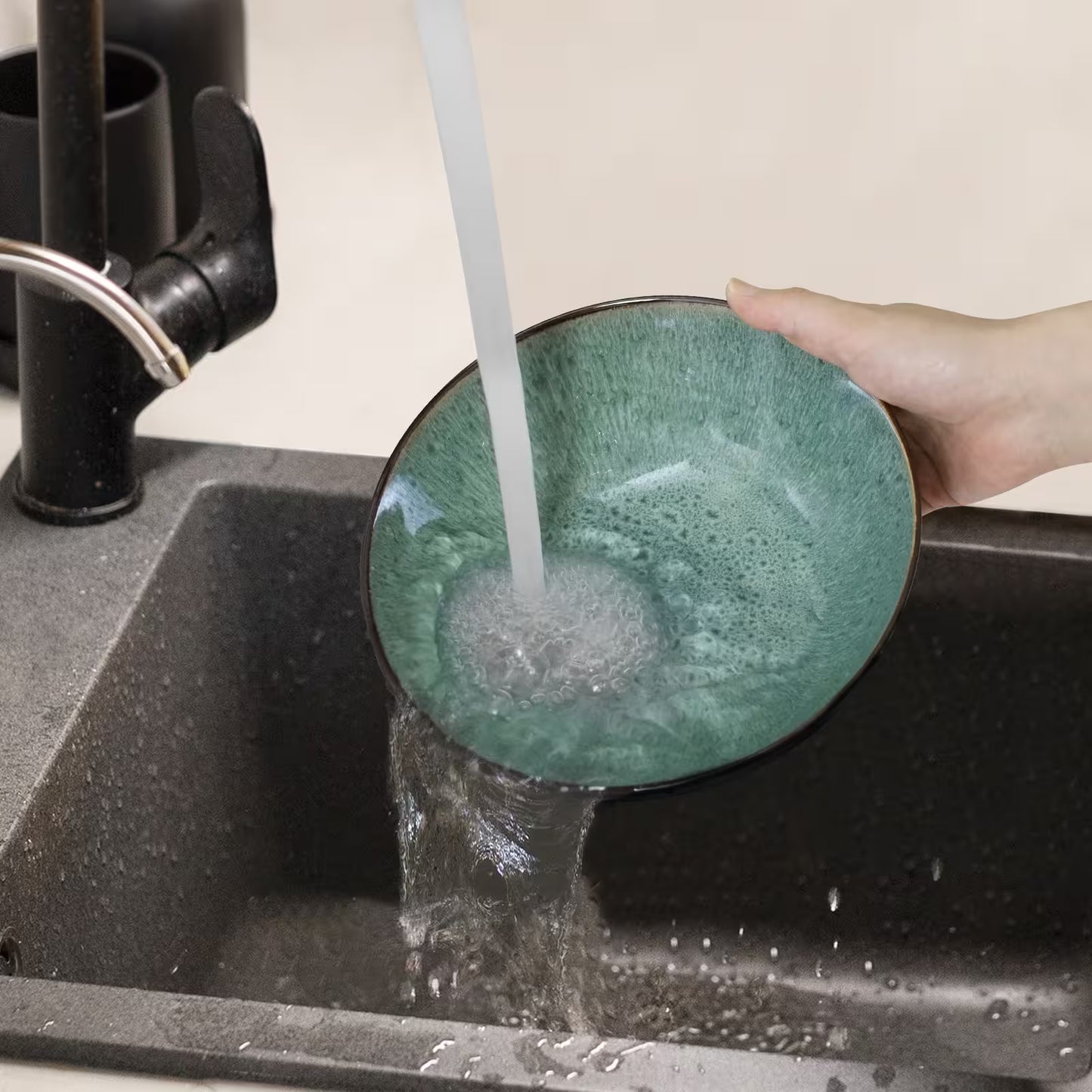 Person washing a green ceramic bowl under running water in a kitchen sink.