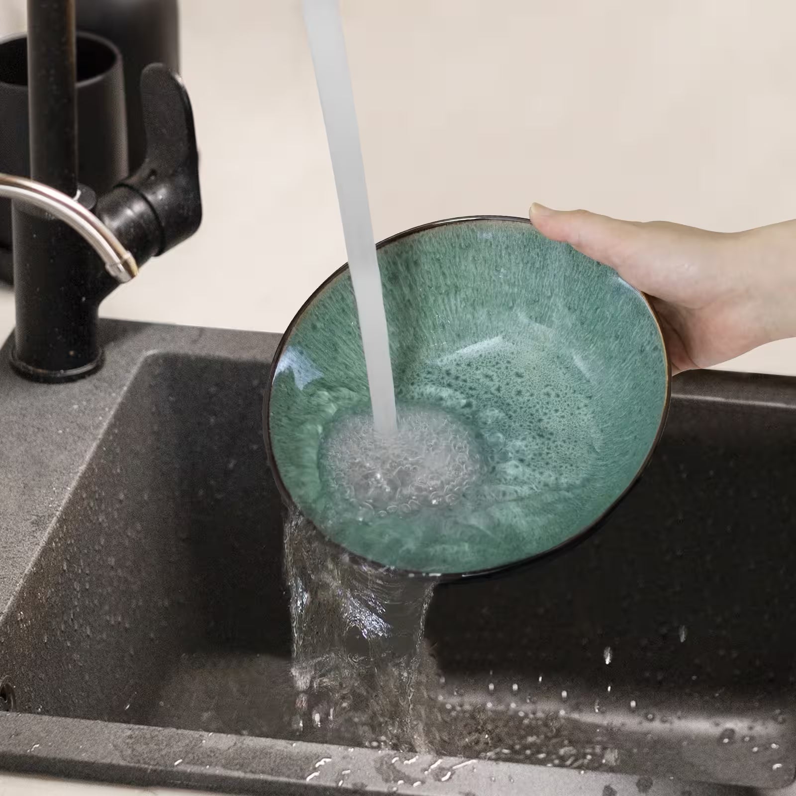 Person washing a green ceramic bowl under running water in a kitchen sink.