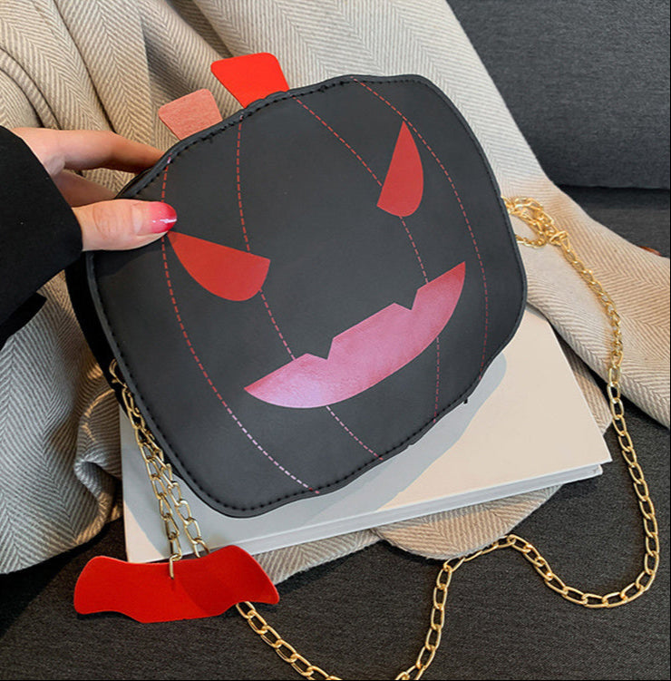 Pumpkin-shaped handbag with a gold chain held by a person.