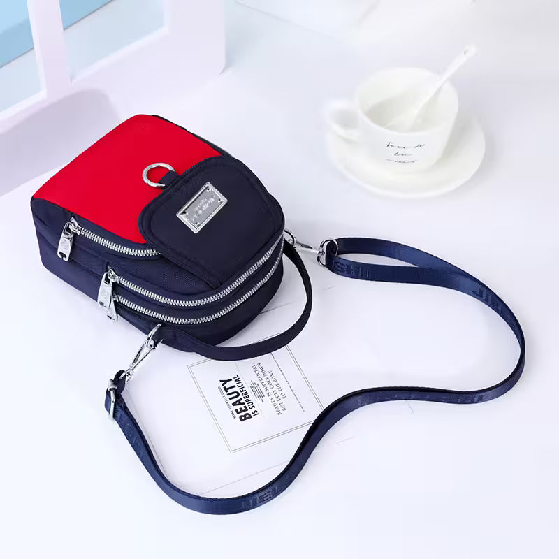 Two-tone red and navy crossbody bag on a white surface with a blurred background