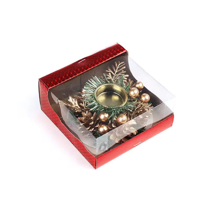Decorative candle holder with greenery and gold elements in a red box on a white background