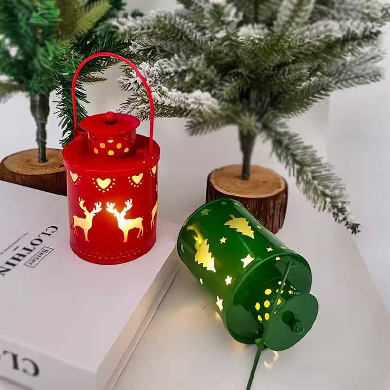 Red and green lanterns with cut-out designs on a white surface with Christmas trees in the background.
