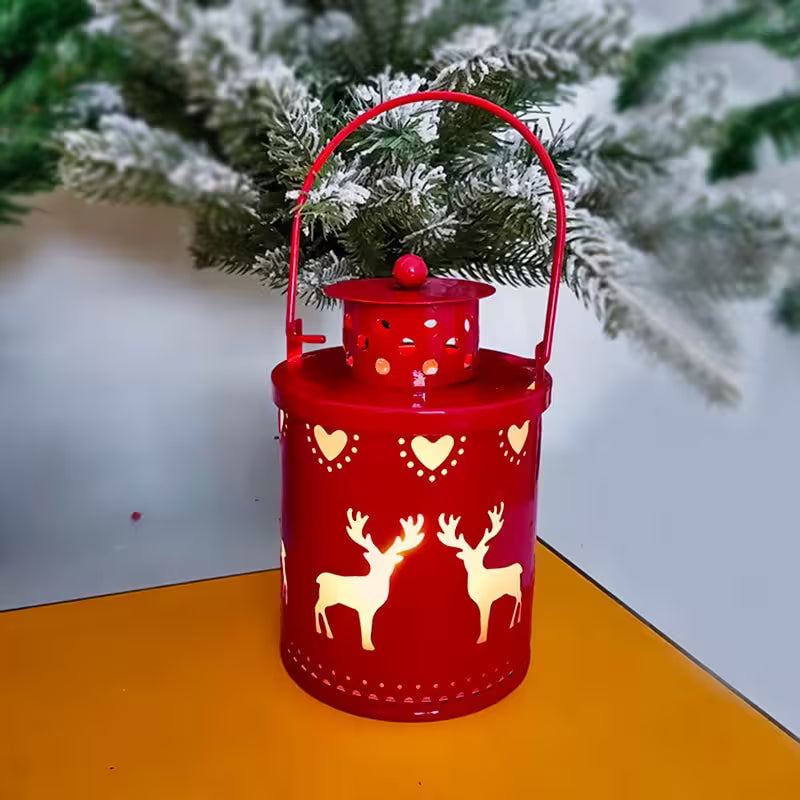 Red lantern with reindeer and heart designs on a yellow surface with a blurred Christmas tree background.