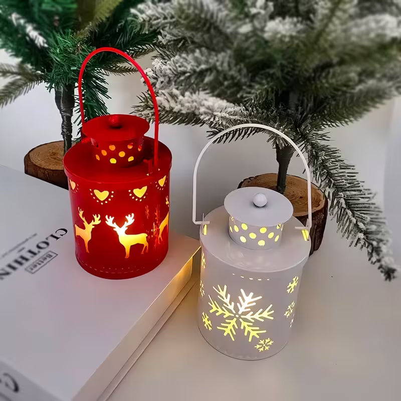Two decorative lanterns, one red with deer designs and one white with snowflake designs, on a surface with a Christmas tree in the background.