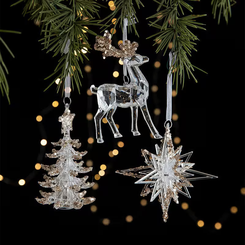 Crystal reindeer, tree, and star ornaments hanging on a Christmas tree with blurred lights in the background.