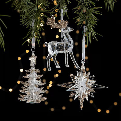 Crystal reindeer, tree, and star ornaments hanging on a Christmas tree with blurred lights in the background.