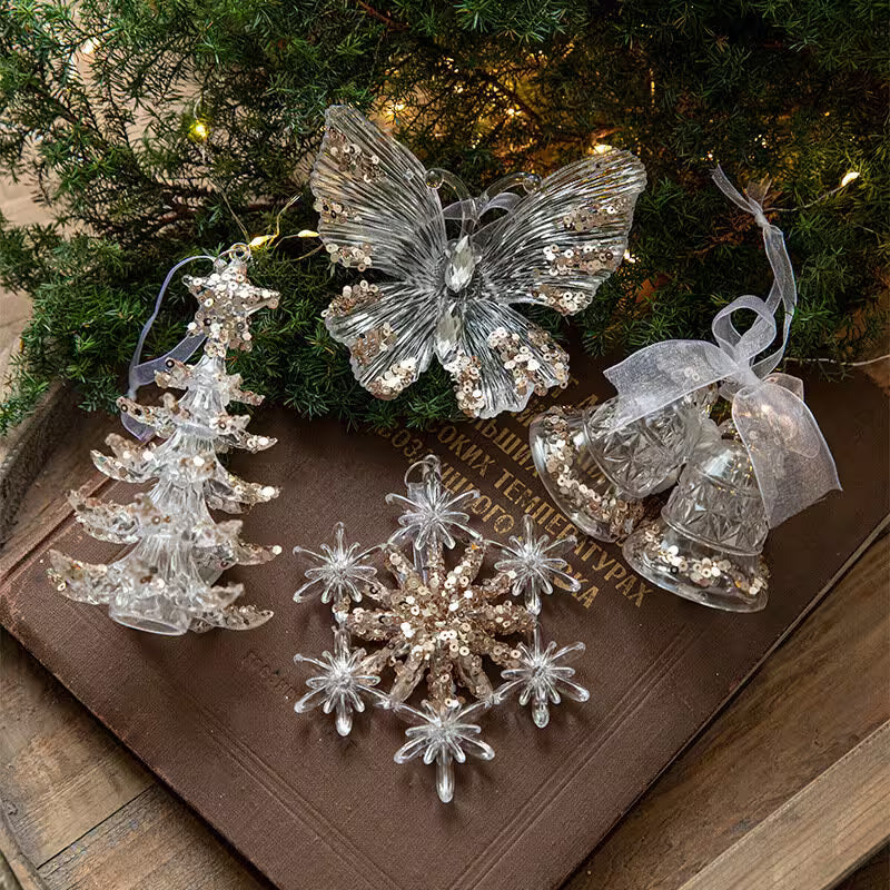 Decorative Christmas ornaments including a butterfly, tree, and snowflake on a wooden surface with a green leafy background.