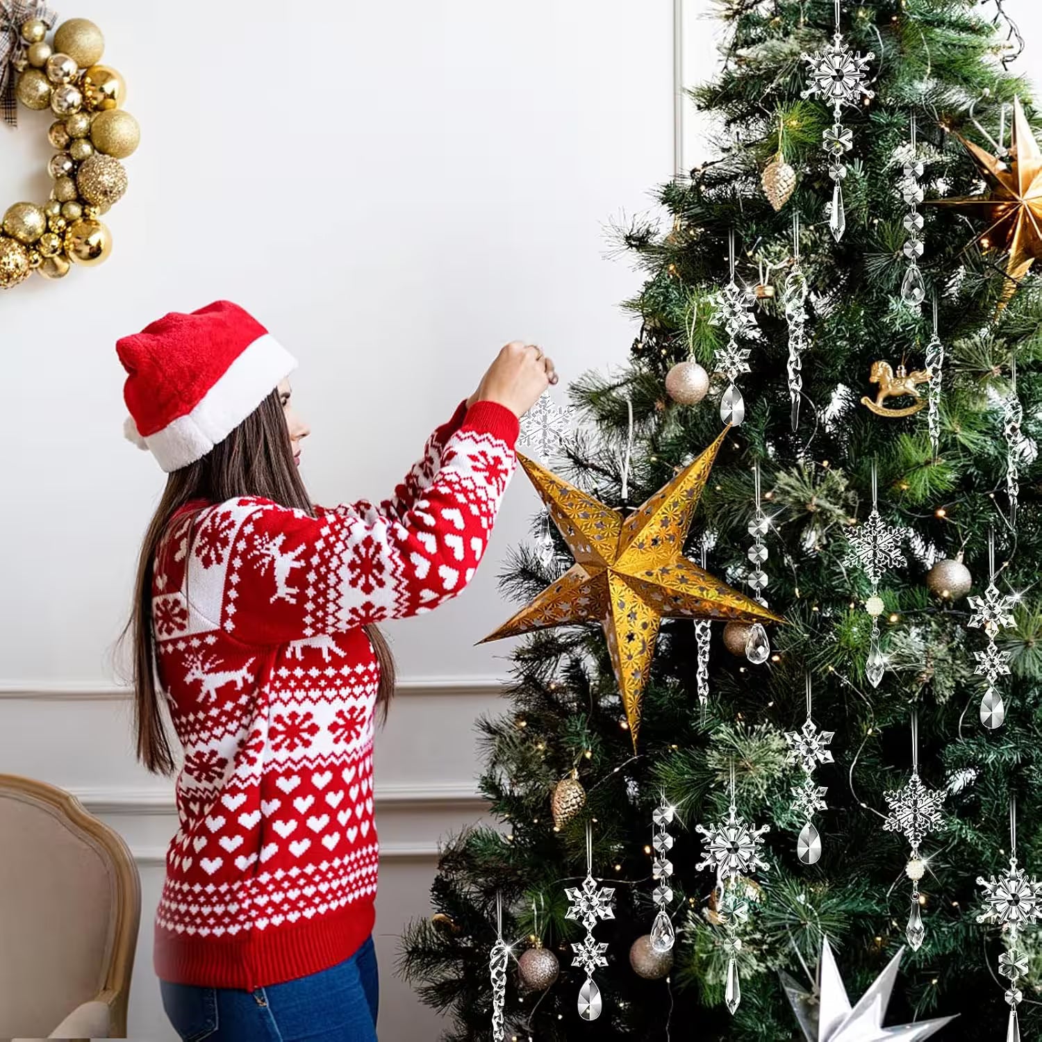 Person decorating a Christmas tree with a gold star ornament, wearing a red and white sweater and Santa hat.
