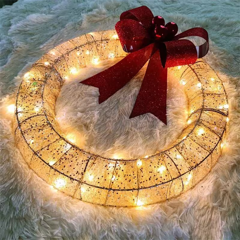 Decorative wreath with lights and a red bow on a fluffy white surface