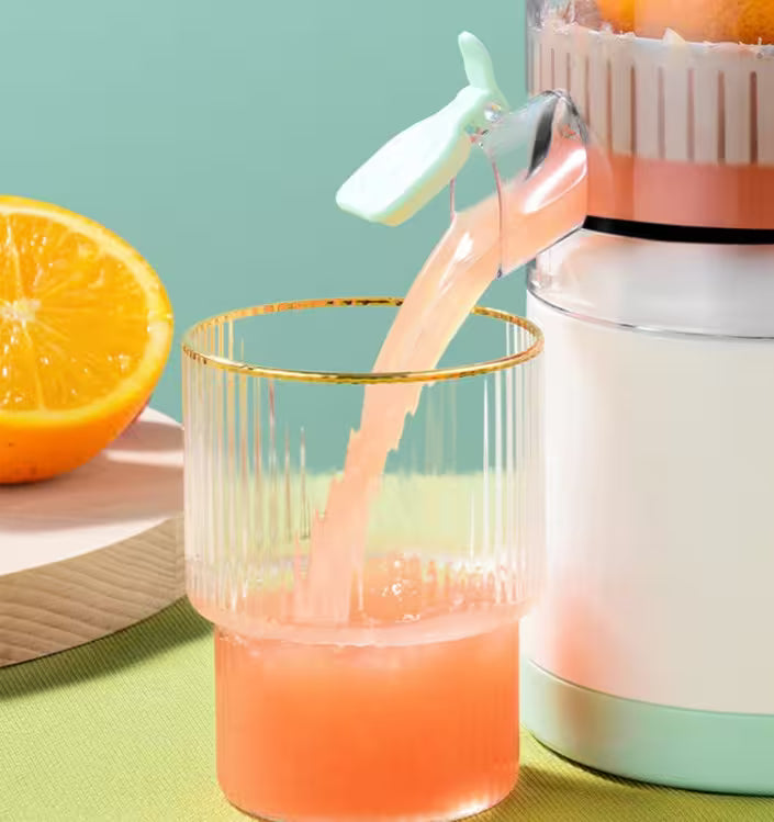 Orange juice being squeezed into a glass with a juicer and half an orange on a green surface.