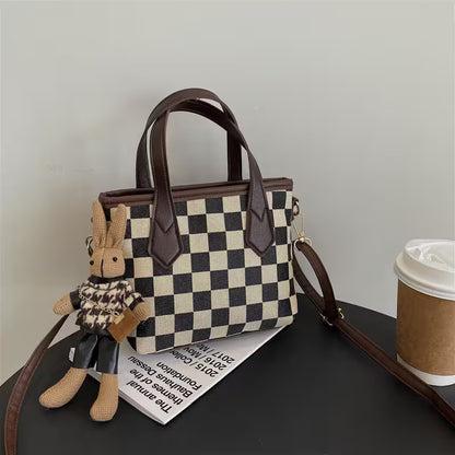 Checkered handbag with a plush toy and a coffee cup on a dark surface