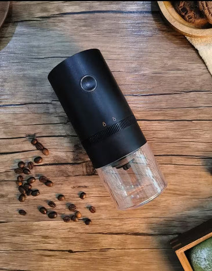 Black and clear coffee grinder on a wooden surface with coffee beans around it