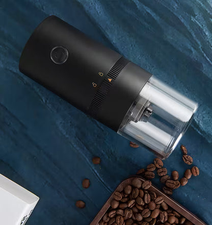 Black coffee grinder with coffee beans on a blue surface