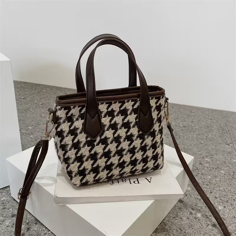 Houndstooth pattern handbag with brown leather accents on a white stand.