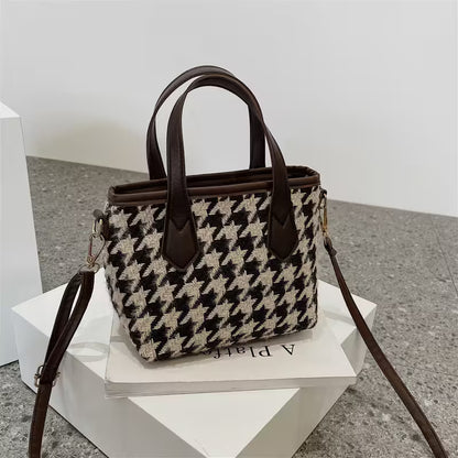Houndstooth pattern handbag with brown leather accents on a white stand.