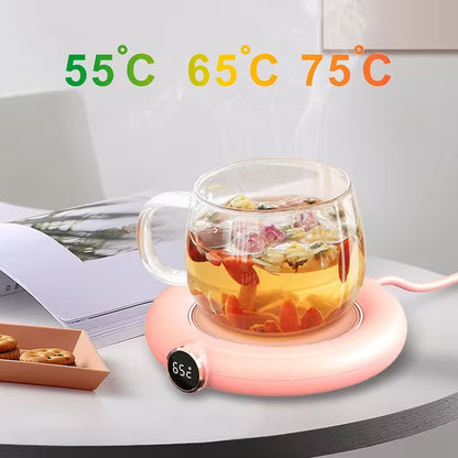 Glass mug with floral tea on a pink heating pad with temperature display, surrounded by cookies and a magazine.
