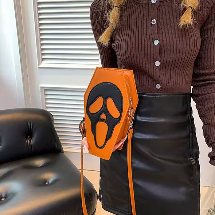 Person holding an orange bag with a black face design in front of a black leather couch.