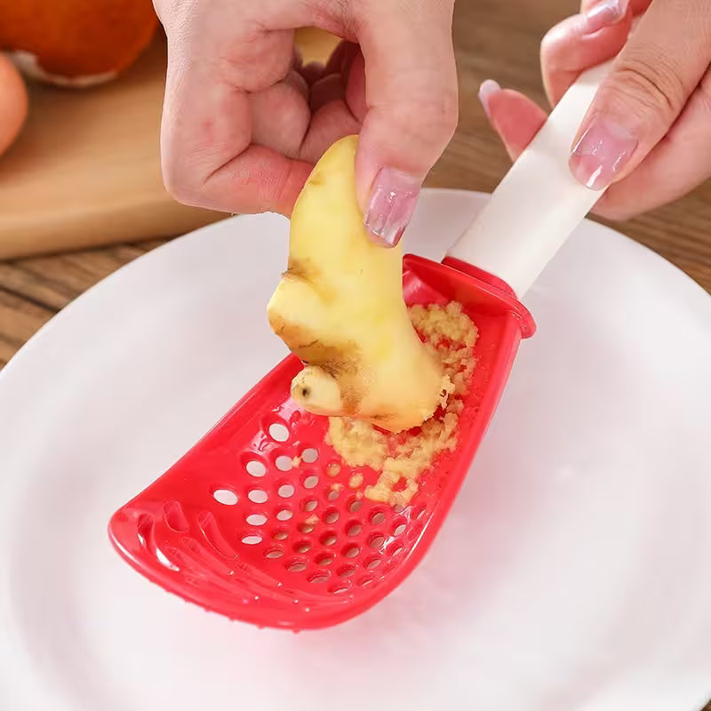 Person using a red garlic press to crush garlic cloves on a white plate.