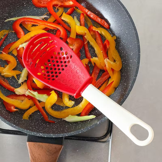 Red spatula stirring colorful bell peppers in a frying pan on a stove.