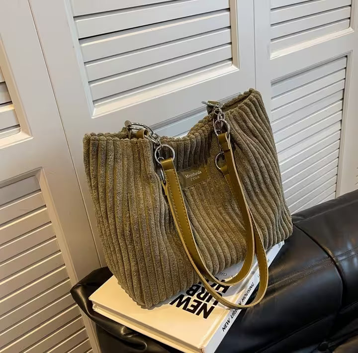 Brown ribbed handbag with a yellow strap on top of a book against a white shutter background