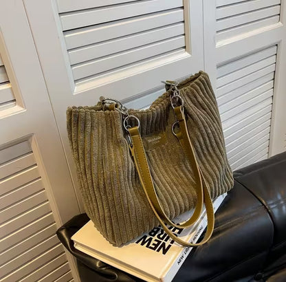 Brown ribbed handbag with a yellow strap on top of a book against a white shutter background