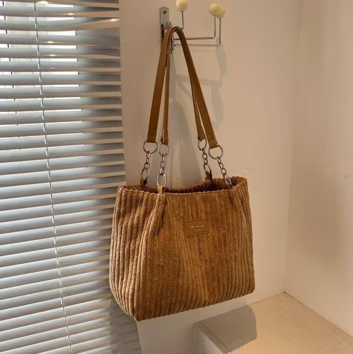Brown textured handbag with a strap hanging on a hook against a neutral wall.