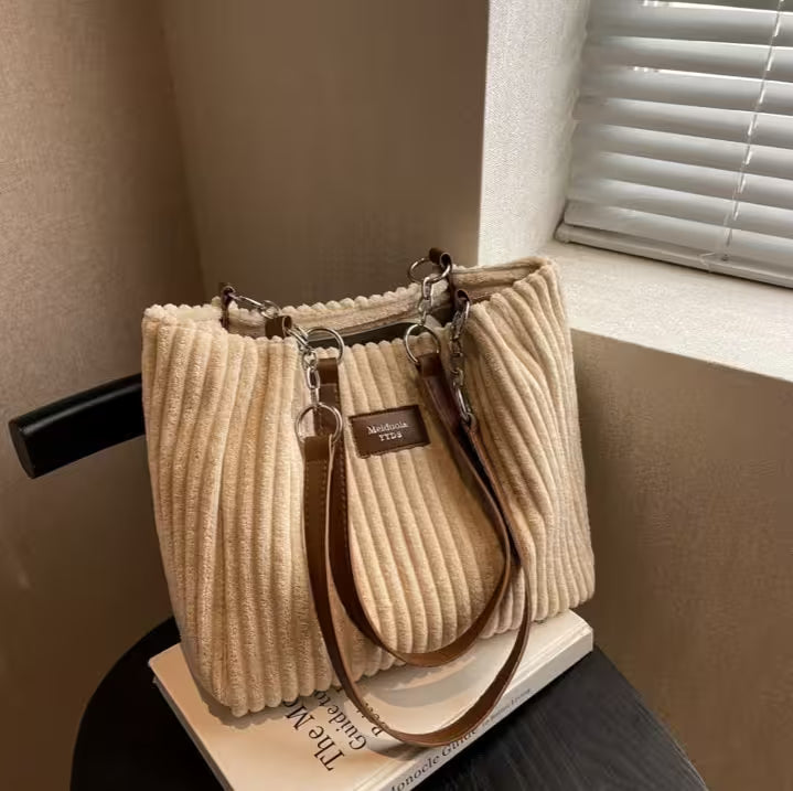 Beige textured handbag with brown strap on a surface near a window.