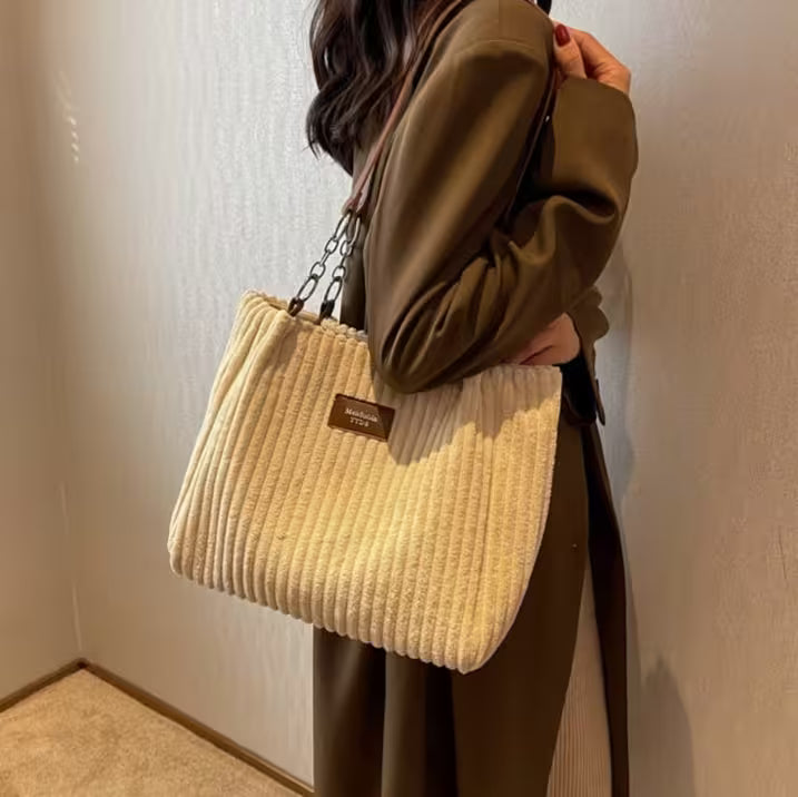Person holding a beige corduroy handbag against a neutral background