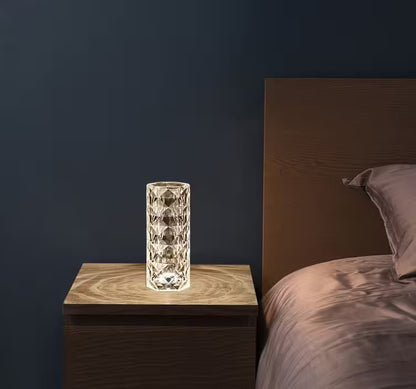 Glass table lamp on a wooden nightstand next to a bed with a dark wall background