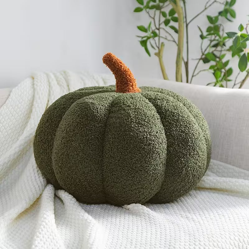 Green textured pumpkin pillow on a white surface with plants in the background