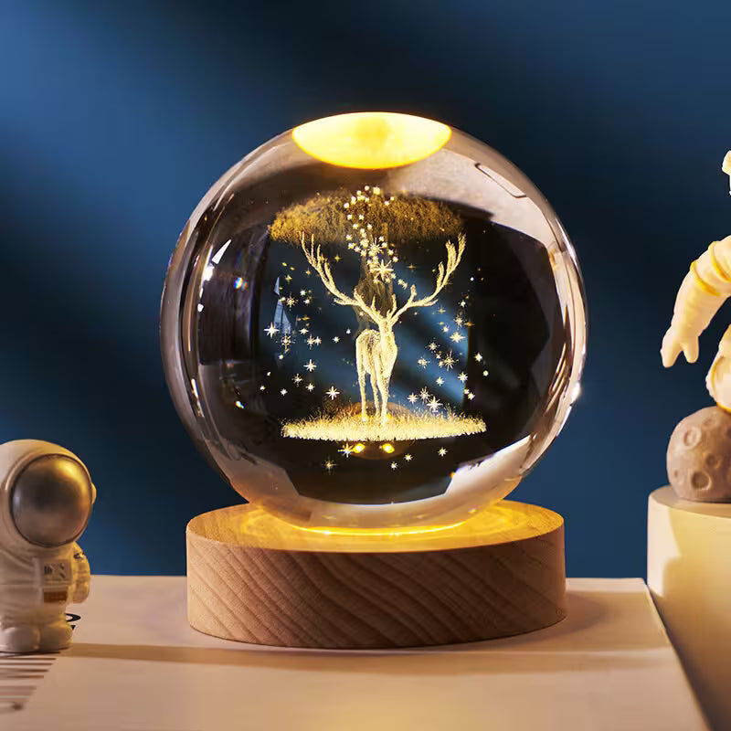 Glass orb with deer design on a wooden base against a dark blue background
