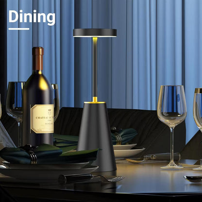 Dining table setting with a bottle of wine, glasses, and a lamp against a blue curtain background.