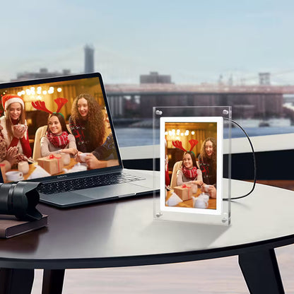Laptop displaying a video call with people in festive attire, next to a transparent photo frame on a table.