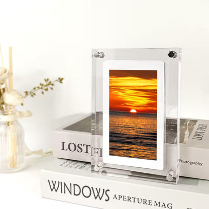 Clear photo frame displaying a sunset over water on a white surface with books and decor items.