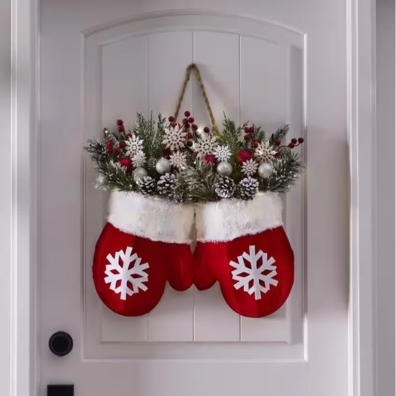 Decorative red mittens with white snowflakes filled with greenery and red berries on a white door.