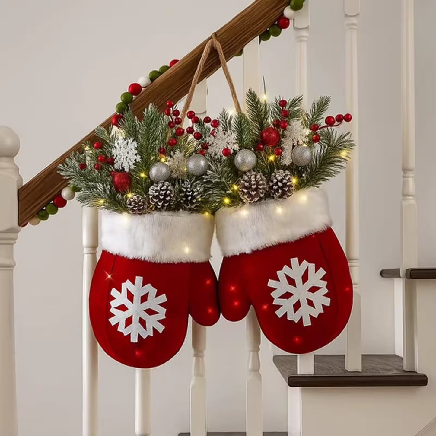Red mitten-shaped stockings with snowflake designs hanging on a staircase decorated with Christmas lights and greenery.