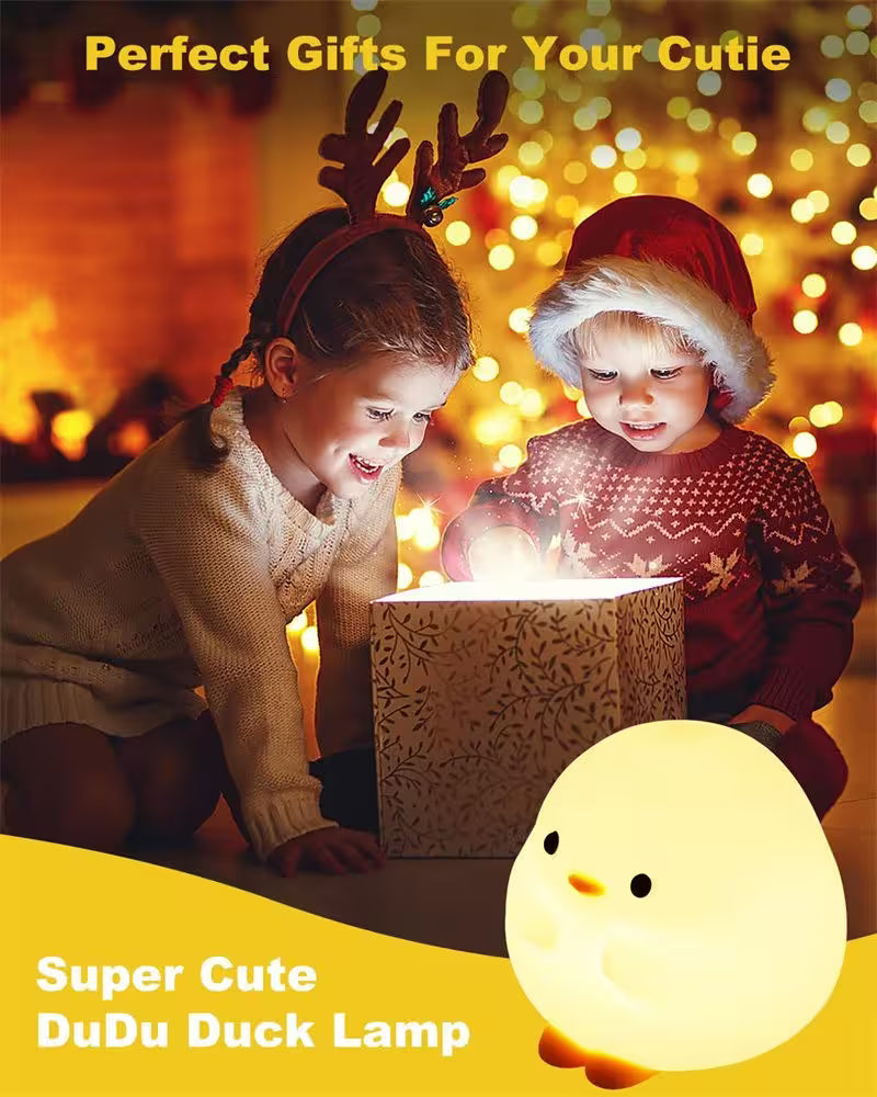 Two children with festive hats looking at a glowing gift box, with a DuDu Duck lamp in the foreground.