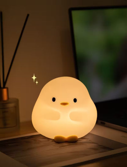 Cute chick-shaped night light on a desk with a blurred laptop and diffuser in the background