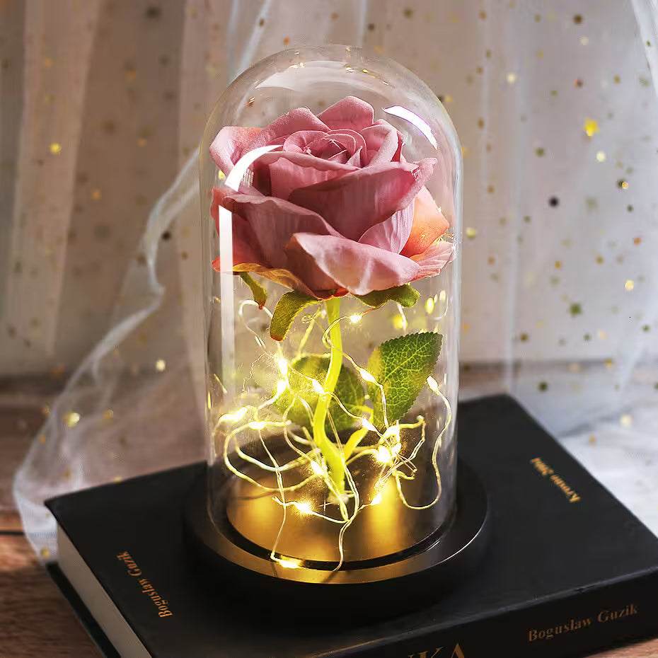 Pink rose in a glass dome with LED lights on a book, against a soft curtain background