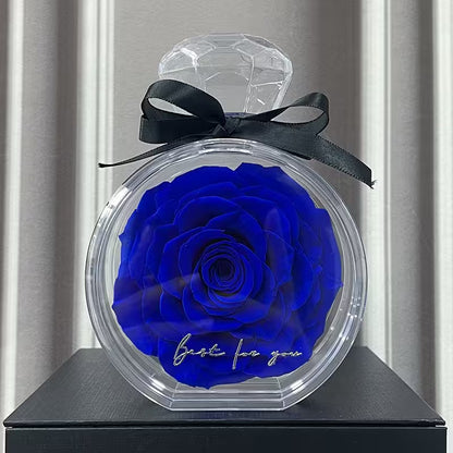 Blue rose in a transparent container with a black bow on a gray surface.
