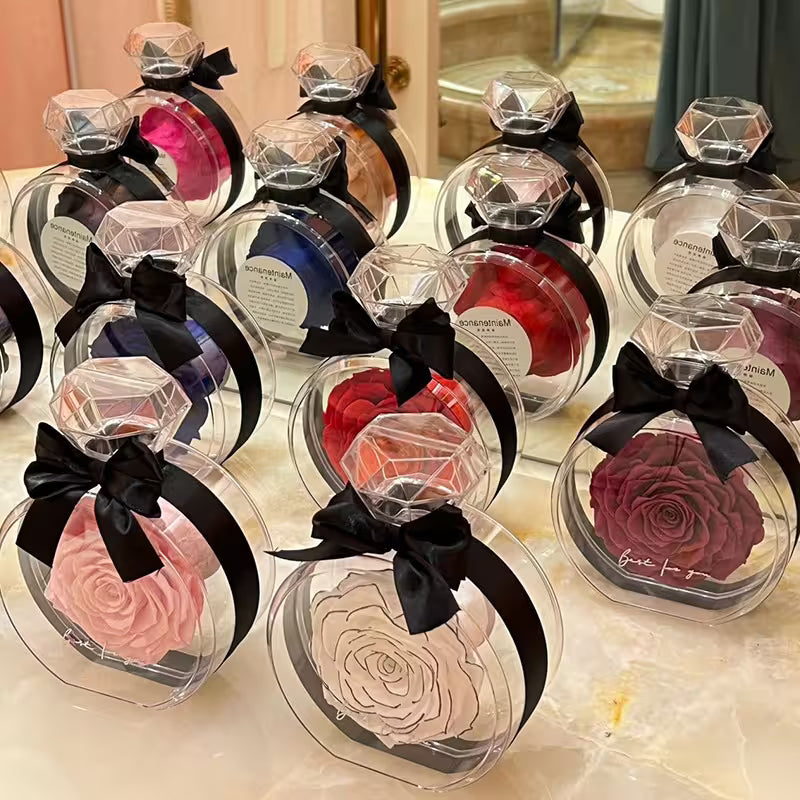 Assorted preserved roses in clear containers with black bows on a reflective surface.